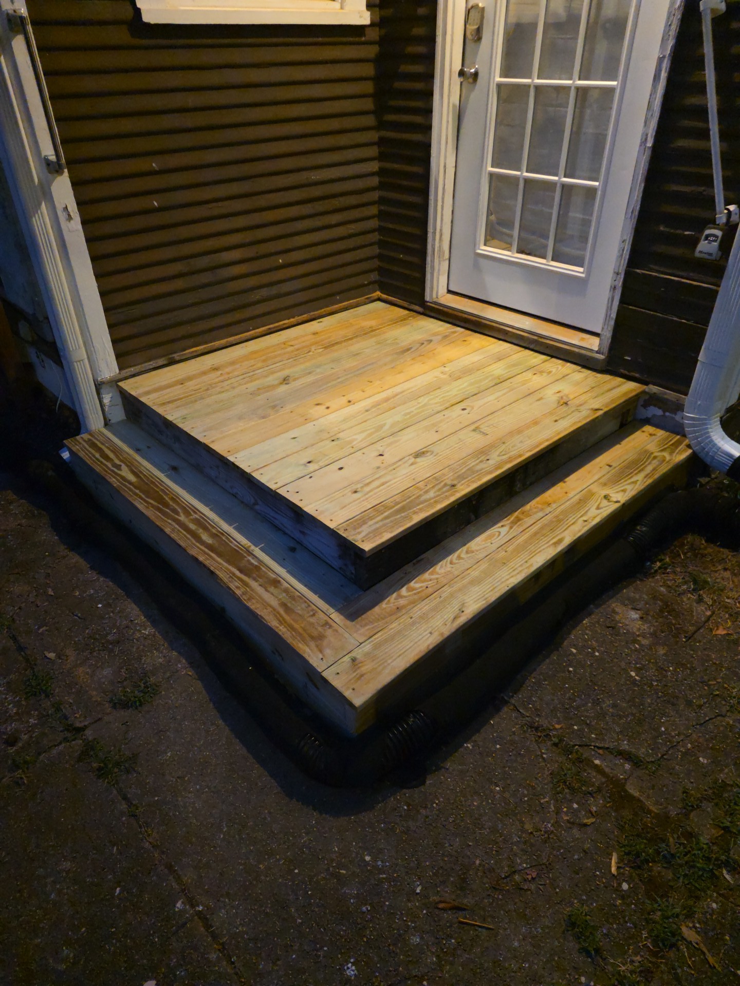 Finished pressure-treated wood landing with a wide wraparound lower step outside an exterior door with dark siding